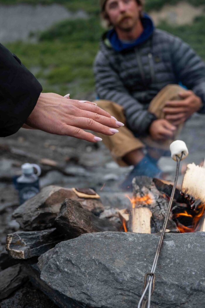 gel tipped nails reaching for marshmallow roasting over fire with person in background watching fire