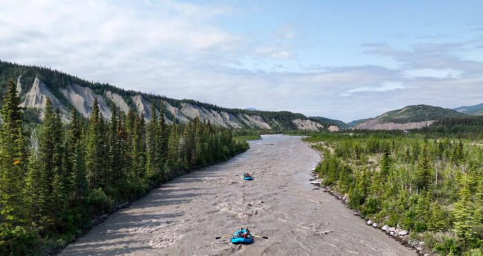 Two blue whitewater rafts paddle down the grey silt of the Matanuska River