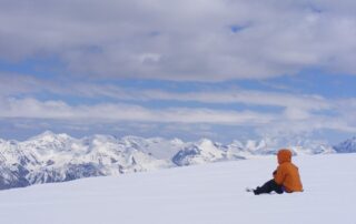 Person in coat on snow looking at snowy mountains