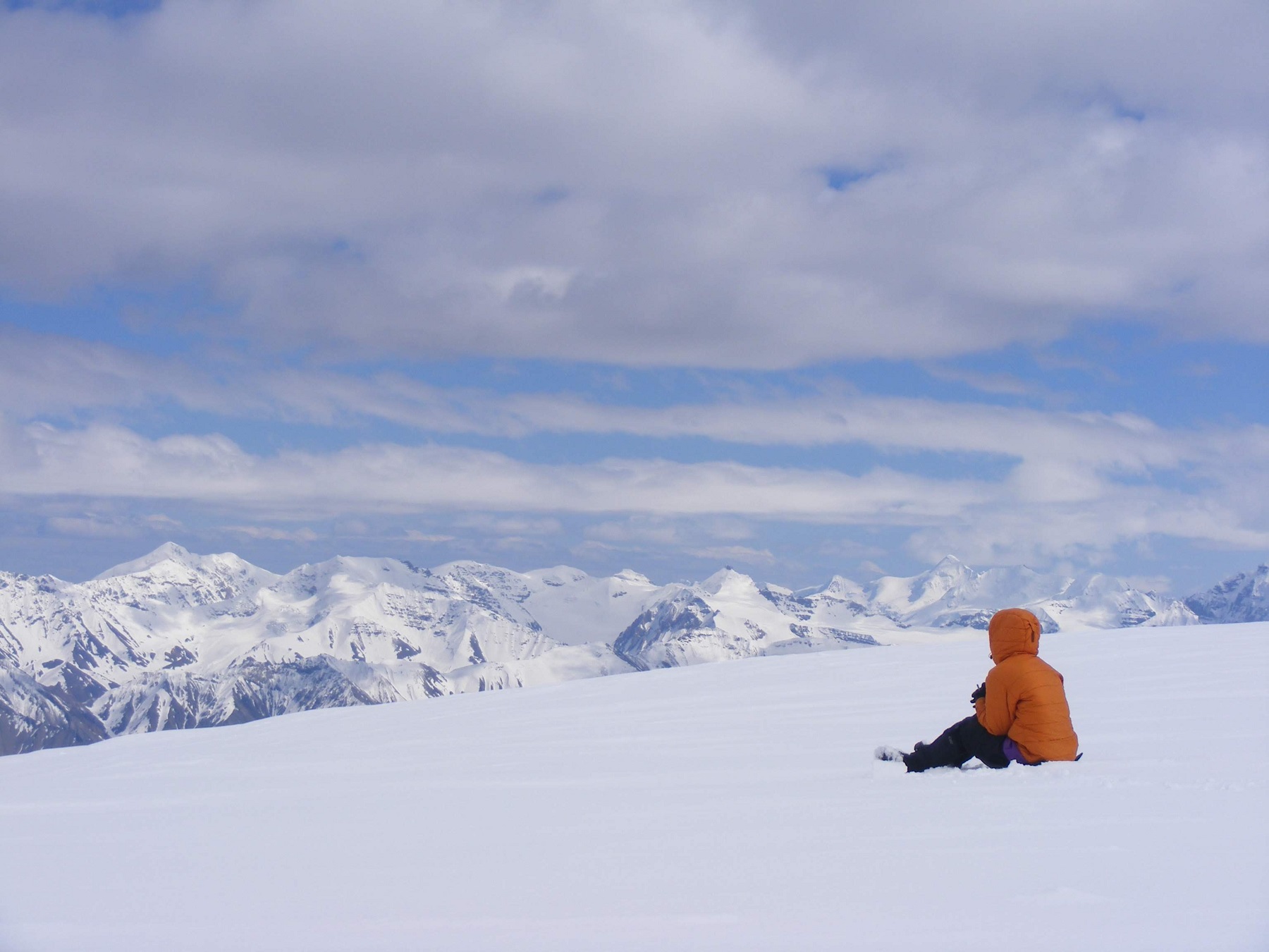 Person in coat on snow looking at snowy mountains