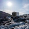bright sun over structure with nearby antennae on glacier ice and moraine