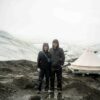 two people in front of canvas tent on glacier moraine with white ice and fog in background