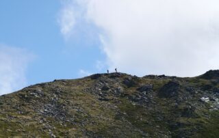 two people hiking on a mountain ridge in the distance